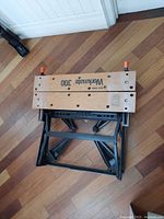 Black & Decker Workmate 300 portable workbench folded flat on wooden floor showing wood top and metal base.