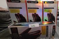 Four boxes of SabotHeat brand battery powered rechargeable heated gloves in black, viewed stacked and arranged on a surface.