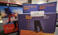 Photo showing packaging of Bernuly electric heated socks with image of a person hiking in winter gear, branding, and battery capacity.