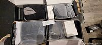 Four boxes containing battery powered rechargeable heated socks, black and grey, with protective packaging, labels, and accessories.