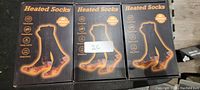 Photo shows three black and grey boxes of heated socks with product features listed on the side.
