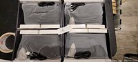 Four pairs of grey and black battery powered rechargeable heated socks, each with a USB charging cable, neatly folded and packaged in a black case.