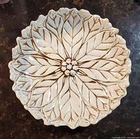 Top down view of the round pottery bowl showing the detailed leaf veins and floral pattern in an off-white glaze with brown lines.
