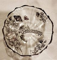 Top-down photo of the clear glass bowl with scalloped edge, silver rim, silver floral designs, and "25th Anniversary" banner inside the bowl.