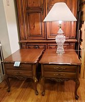 Two wooden end tables side by side with visible bite marks on one leg of the left table and glass lamp with shade on the right table.