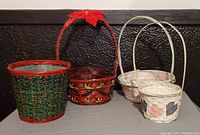 Four wicker baskets arranged on a surface against a black wall, showing the handles and color details of each basket.