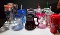 Photo of eleven assorted to-go cups with multiple colored lids and straws, various holiday and branding themes.