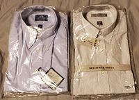 Front view of two packaged men's dress shirts, one light purple and one white with thin stripes.
