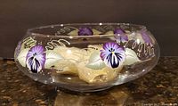 Side view of the painted glass bowl showing purple flowers and gold accents, with floating candles inside.