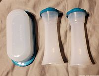 Photo showing two translucent white shakers with teal lids along with a white butter dish base and teal lid, laid on a cloth surface.