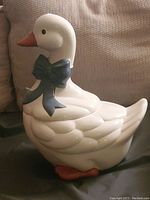 Side view of the white ceramic goose cookie jar showing raised relief details and dark blue bow.