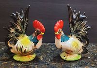 Front view of two colorful vintage ceramic rooster figurines with detailed hand-painted feathers and bases