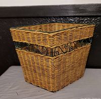 Side angle view of the square wicker basket showing woven wicker body and decorative black wire scroll detail near the top.