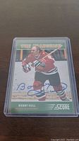 Front of the Bobby Hull autographed hockey card showing him in Chicago Blackhawks uniform with his signature in blue ink, inside a protective plastic sleeve.
