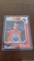Front of the Connor McDavid rookie card in protective case showing image of McDavid in Edmonton Oilers uniform with 'Rookie Card' and 'Memorable Moments' labeling.