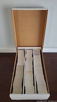 Wide shot of open cardboard box with three compartments filled with stacks of sports cards.