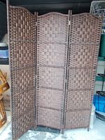 Three-panel brown woven resin privacy screen with hinged folding sections and arched tops, standing freely.