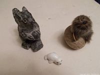 Three animal figurines displayed together including soapstone squirrel, fur seal on rock, and white china seal pup.