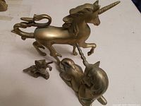 Three brass unicorn figurines on a white surface, including two larger standing unicorns and one small lying unicorn.