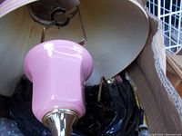 Close-up photo showing pink ceramic lamp base with brass accents, light pink fabric shade with wear and tear visible