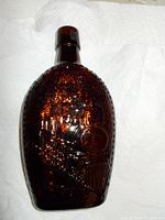 Front relief detail of brown blown glass commemorative bottle featuring Canadian Railway imagery