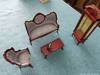Miniature Victorian style settee, armchair, coffee table, and upright glass display cabinet set on blue fabric surface