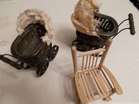 Two dark wicker doll prams with black iron wheels and bracing, and a light wicker rocker with missing seat board shown together on floor.