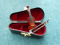 Miniature violin displayed inside open black leather case lined in red velvet with bow placed above violin.