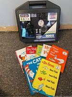 Photo of six Dr. Seuss kids books stacked in front of a black plastic case containing 900X 25-piece microscope kit showing items included and condition