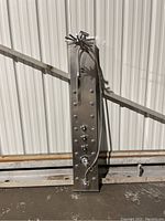 Full front angled view of stainless steel spa shower panel showing overhead shower head, multiple water nozzles, and handheld shower hose.