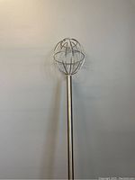 Photo showing the full length of the stainless steel industrial whisk with spherical wire head and long handle against a plain background.