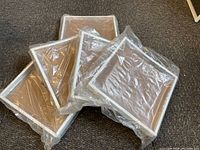 Five square t-shirt display boxes stacked on carpeted floor, wrapped in clear plastic covers.