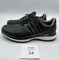 Side profile of black Adidas Tour 360 golf shoes showing synthetic leather construction, Adidas stripes, and branding on the side midsole.