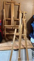 Three wooden art easels arranged side-by-side with two smaller easels in front and a larger easel behind.