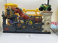 Front view of the entire dinosaur play set showing the large red and green T-Rex in an enclosure, purple dinosaur below, lookout tower with two action figures, green quad bike on rock platform, and dinosaur-themed stickers.