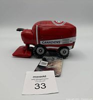 Side view of red vinyl Zamboni toy with Montreal Canadiens logo and black wheels on white background, tag visible.