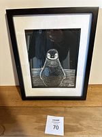 Full frontal photo of the framed penguin print showing the entire artwork, frame, and label on the table.