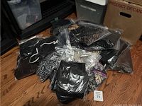 Multiple resealable plastic bags containing assorted used women's clothing items such as sequined tops, printed dresses, and leggings mainly in dark and multicolor fabrics.