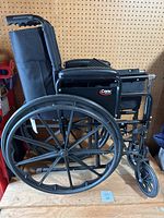 Side view of folded black Cartex wheelchair showing large rear wheel and folded frame
