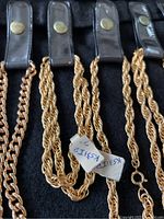 Close-up of electroplated gold-tone twisted rope chains hung on black leather-like display straps with button snaps and price tags.