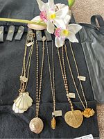 Photo of six necklaces on black display showing varied seaside-themed pendants including scallop shells, detailed shell, and coral cluster.