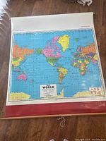 Full view of vintage Cram World Map laid out showing continents, oceans, and a red wooden roller at the bottom with pull cord.