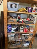 Wood shelving filled with painting and workshop supplies such as paint cans, varnish, oils, and small bottles.