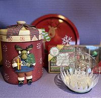 Front view of all items: moose cookie jar, red reindeer serving tin, light-up ornament, wine napkins