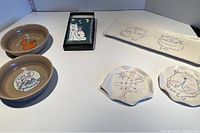 All items displayed including two brown ceramic pet bowls, rectangular plate, two small irregular plates, and cat light switch cover