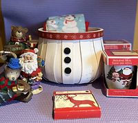 Overall lot showing Santa candle holder snowman, two holiday bear figurines, boxed mugs, boxed coaster set, and folded holiday tea towels