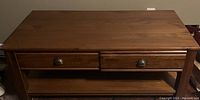 Front view of the solid wood coffee table showing two drawers with metal cup handles and bottom shelf.