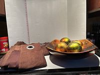 Curtain panels folded with visible metal grommets beside wooden decorative bowl with five decorative balls