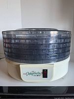 Mr. Coffee food dehydrator assembled with 5 clear trays stacked on white base. Power indicator light and on/off switch visible on base.