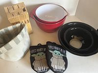 Side view of the kitchen items including mixing bowls, oven mitts, knife block, fabric container, and black serving bowls on a shelf.